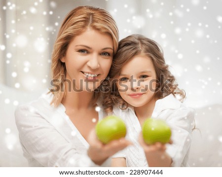 family, winter, healthy food and people concept - happy mother and daughter holding green apples at home