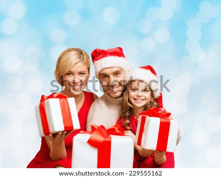 christmas, holidays,  family and people concept - happy mother, father and little girl in santa helper hats with gift boxes over blue lights background