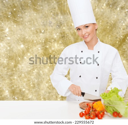 cooking, holidays, people and food concept - smiling female chef chopping vegetables over yellow lights background