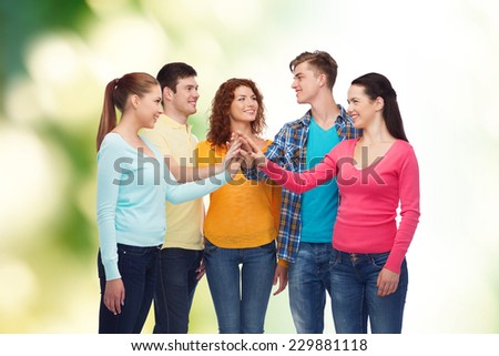 friendship, ecology, teamwork, gesture and people concept - group of smiling teenagers making high five over green background