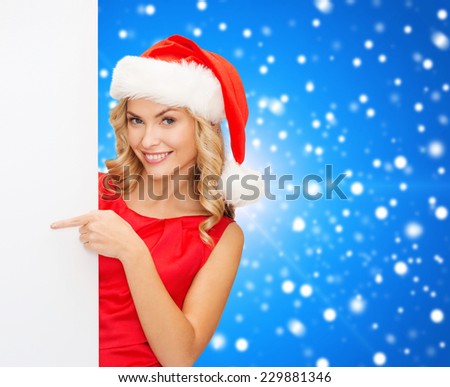 winter holidays, christmas, advertising and people concept - smiling young woman in santa helper hat with white blank billboard over blue snowy background