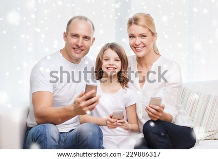 family, home, technology and people concept - smiling mother, father and little girl with smartphones over snowflakes background