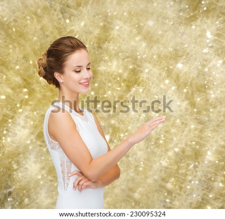 engagement, celebration, wedding and people concept - smiling woman in white dress wearing diamond ring over yellow lights background