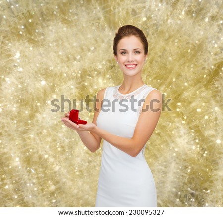 wedding, love, engagement and people concept - smiling woman in white dress holding red gift box with diamond ring over yellow lights background