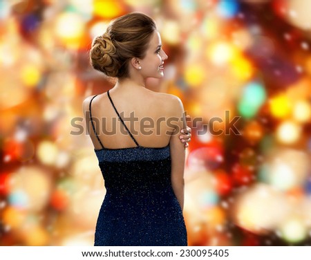 people, holidays and christmas and people concept - smiling woman in evening dress over red lights background from back