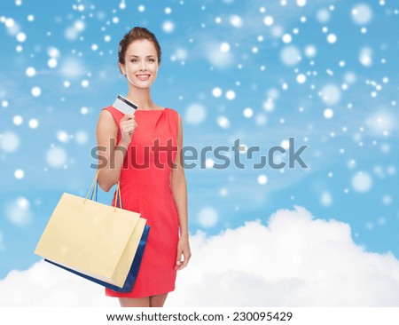 shopping, sale, christmas and holiday concept - smiling elegant woman in red dress with shopping bags and plastic card over blue sky with cloud and snow background