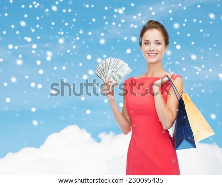shopping, sale, christmas and holiday concept - smiling elegant woman in red dress with shopping bags and dollars over blue sky with cloud and snow background