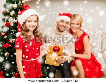 family, christmas, winter holidays, childhood and people concept - smiling family in santa helper hats decorating christmas tree at home