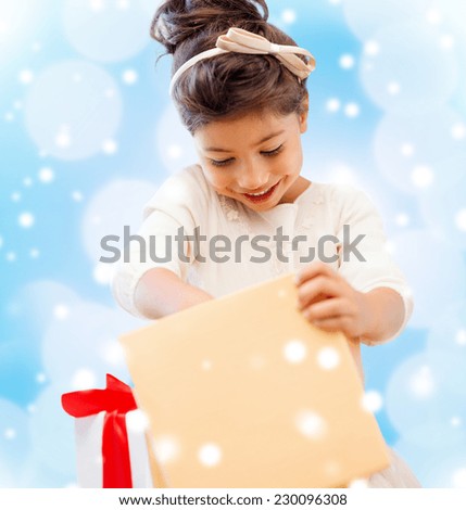 holidays, christmas, childhood and people concept - smiling little girl with gift box over blue lights background