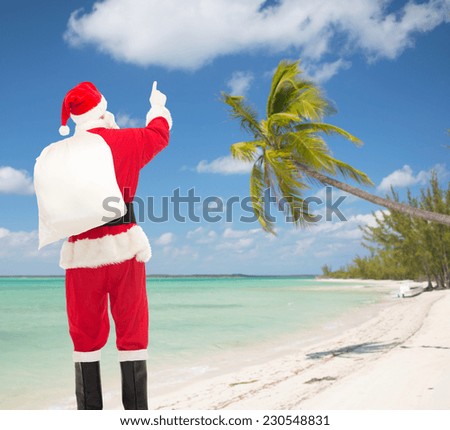 christmas, holidays, travel and people concept - man in costume of santa claus with bag pointing finger from back over tropical beach background
