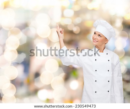 cooking, advertisement and people concept - smiling female chef, cook or baker pointing finger up to something over holidays lights background