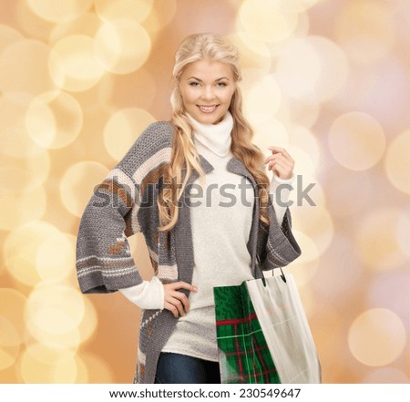 happiness, winter holidays, christmas and people concept - smiling young woman in winter clothes with shopping bags over beige lights background