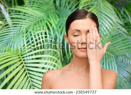beauty, people and health concept - smiling young woman covering half of face with hand over palm tree leaves background