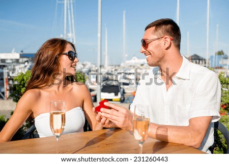 love, dating, people and holidays concept - smiling couple wearing sunglasses with champagne and small red gift box looking to each other at cafe