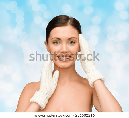 beauty, winter, people and health concept - smiling young woman in white mittens over blue lights background