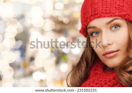 happiness, winter holidays, christmas and people concept - close up of smiling young woman in red hat and scarf over lights background