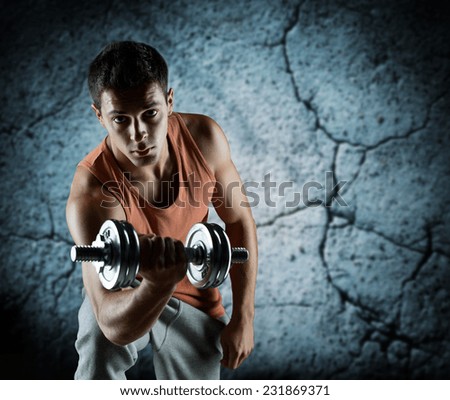 sport, bodybuilding, training and people concept - young man with dumbbell flexing biceps over concrete wall background