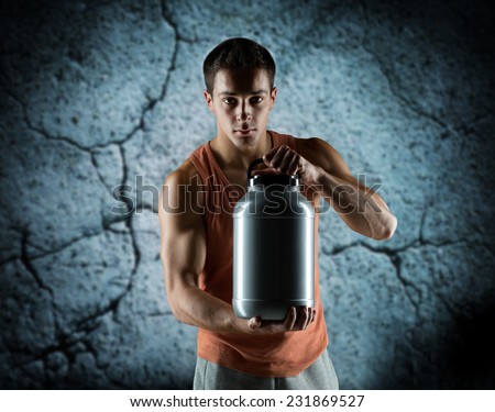 sport, bodybuilding, strength and people concept - young man standing holding jar with protein over concrete wall background