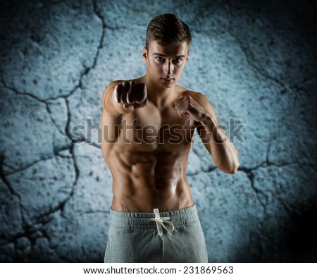 sport, competition, strength and people concept - young man in fighting or boxing position over concrete wall background