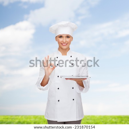 cooking, technology and people concept - smiling female chef, cook or baker with tablet pc computer over blue sky and grass background