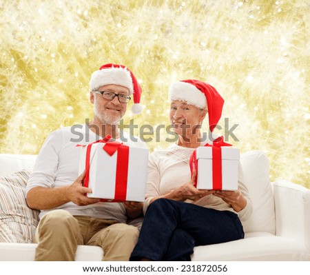 family, holidays, christmas, age and people concept - happy senior couple in santa helper hats with gift boxes over yellow background