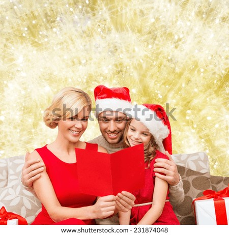 christmas, holidays, family and people concept - happy mother, father and little girl in santa helper hats with gift boxes reading geeting card over yellow lights background