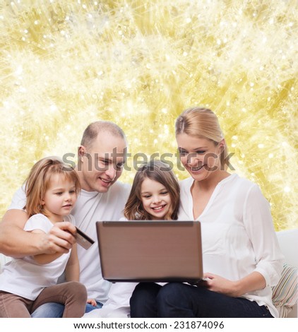 family, holidays, shopping, technology and people - happy family with laptop computer and credit card over yellow lights background