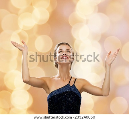 people, happiness, holidays and glamour concept - smiling woman raising hands and looking up over beige lights background