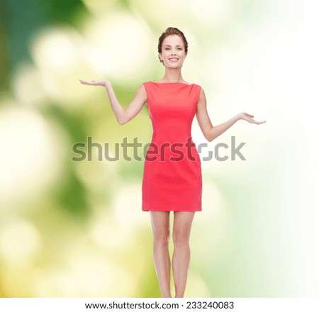 advertising, holidays and people concept - smiling young woman in red dress holding something on palm of her hands over green background