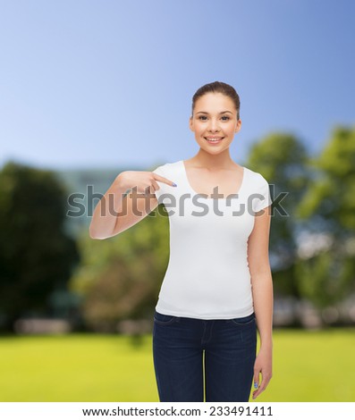 gesture, advertising, summer vacation and people concept - smiling young woman in blank white t-shirt pointing finger on herself over park background