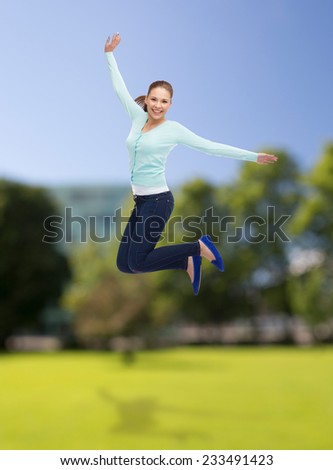 happiness, freedom, summer, nature and people concept - smiling young woman jumping in air over park background