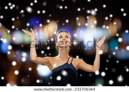 people, happiness, holidays and christmas concept - smiling woman raising hands and looking up over snowy night city lights background