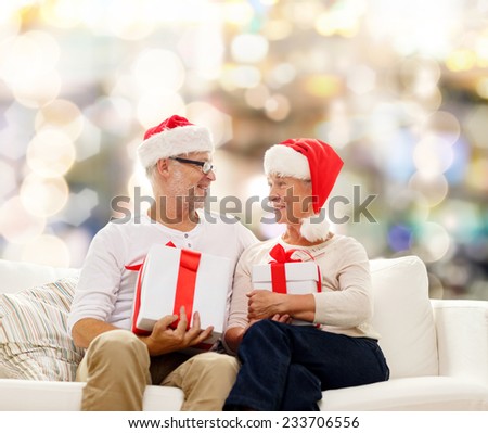 family, holidays, christmas, age and people concept - happy senior couple in santa helper hats with gift boxes over lights background