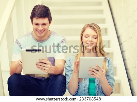education and technology concept - smiling students with tablet pc computer sitting on staircase