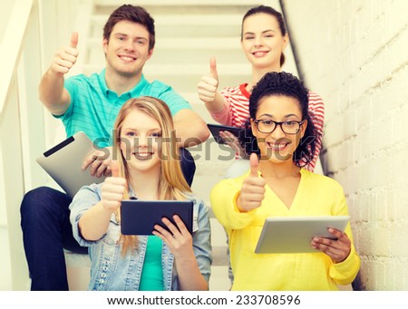 education and technology concept - smiling students with tablet pc computer sitting on staircase and showing thumbs up