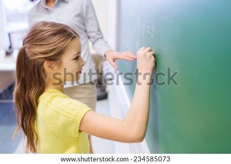 education, elementary school, learning, math and people concept - little smiling schoolgirl writing numbers on green chalk board in classroom