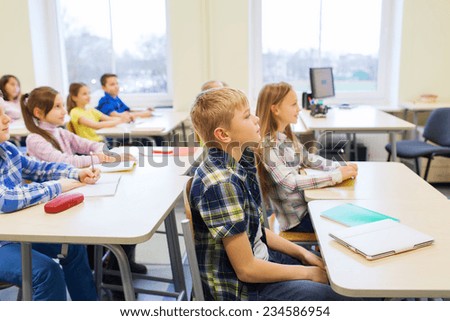 education, elementary school, learning and people concept - group of school kids with notebooks sitting in classroom