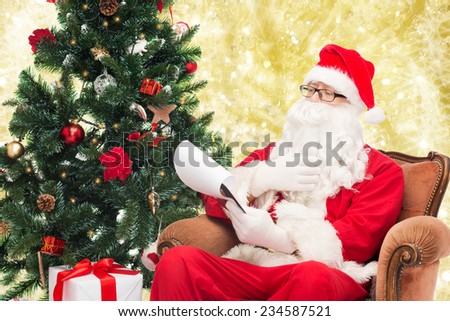 christmas, holidays and people concept - man in costume of santa claus with notepad and pen over yellow lights background