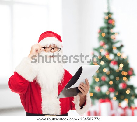 christmas, holidays and people concept - man in costume of santa claus with notepad over living room and tree background