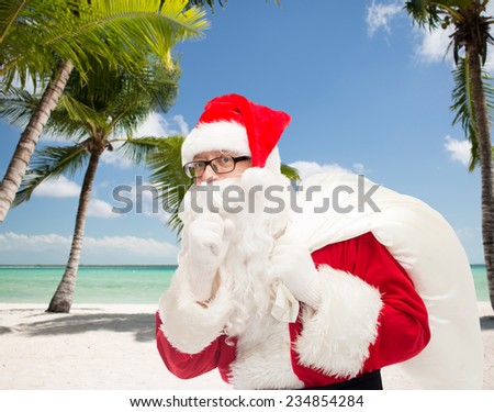 christmas, holidays, travel and people concept - man in costume of santa claus with bag making hush gesture over tropical beach background