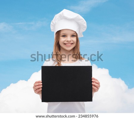 cooking, childhood, advertisement and people concept - smiling little chef girl, cook or baker with blank black paper over blue sky with cloud background