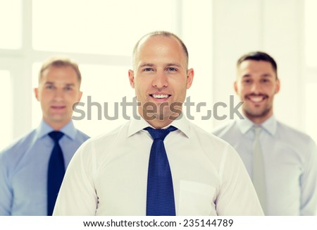 business and office concept - smiling businessman in office with team on the back