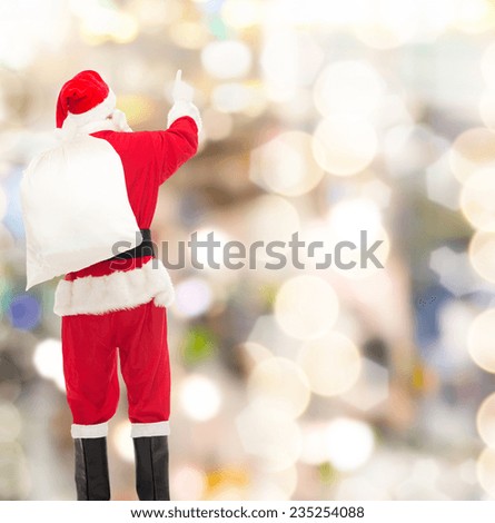 christmas, holidays and people concept - man in costume of santa claus with bag pointing finger from back over yellow lights background over lights background