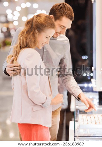 sale, consumerism, shopping and people concept - happy couple choosing engagement ring at jewelry store in mall