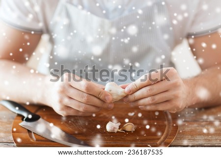 cooking, food, people and home concept - close up of male hands taking off peel of garlic on cutting board in kitchen