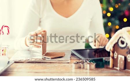 cooking, people, christmas and technology concept - close up of smiling woman with tablet pc computer making gingerbread houses at home