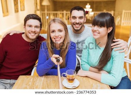 people, leisure, friendship and technology concept - group of happy friends with selfie stick taking picture and drinking tea at cafe