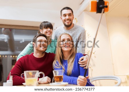 people, leisure, friendship and technology concept - group of happy friends with smartphone selfie stick taking picture and drinking tea at cafe