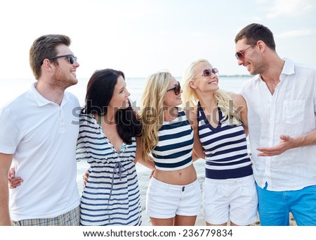 summer, holidays, sea, tourism and people concept - group of smiling friends in sunglasses talking on beach