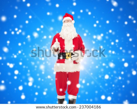 christmas, holidays, gesture and people concept- man in costume of santa claus showing thumbs up over blue snowy background